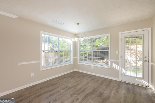 unfurnished dining area featuring baseboards, wood finished floors, a notable chandelier, and visible vents