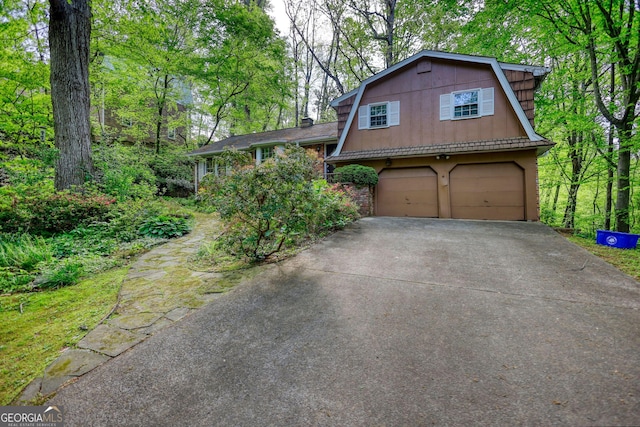 view of front of property with concrete driveway, an attached garage, a gambrel roof, and stucco siding