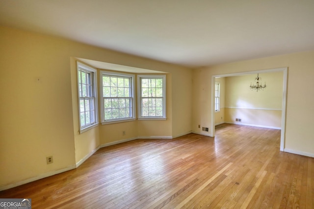 spare room with light wood-type flooring, a wealth of natural light, and a notable chandelier