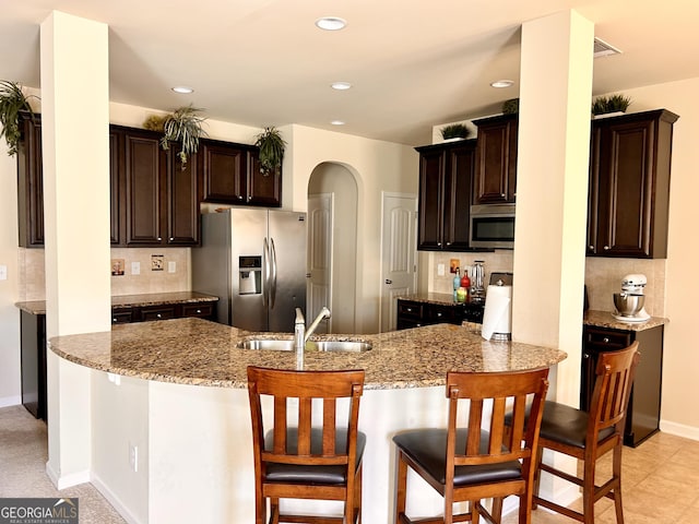kitchen with arched walkways, dark brown cabinetry, a sink, and stainless steel appliances
