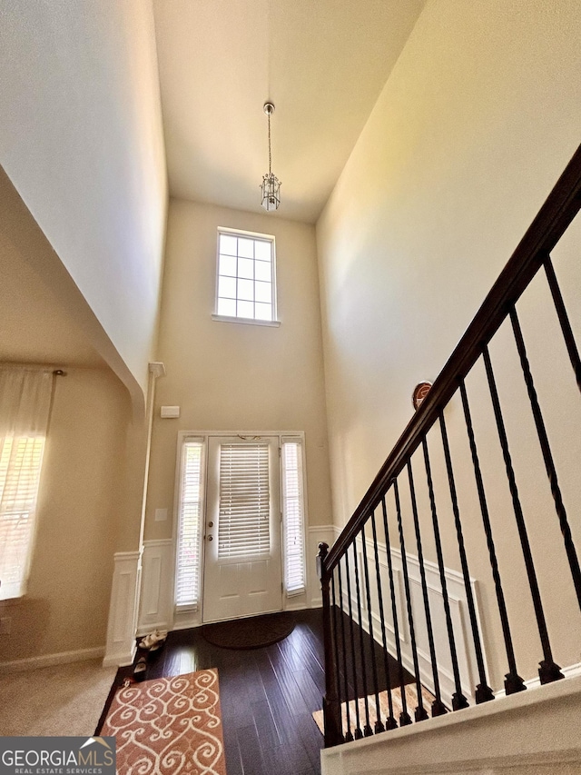 foyer with a notable chandelier, a high ceiling, stairway, wood finished floors, and a wainscoted wall