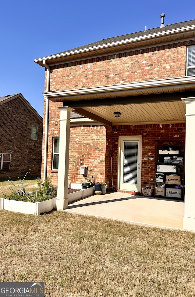 back of house featuring a lawn, a patio area, and brick siding
