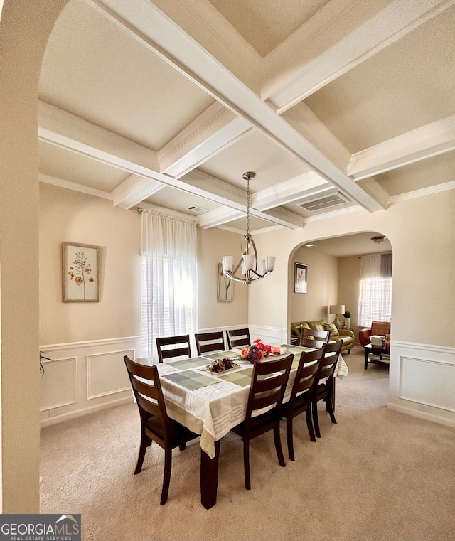 dining space with arched walkways, a decorative wall, beamed ceiling, coffered ceiling, and light carpet