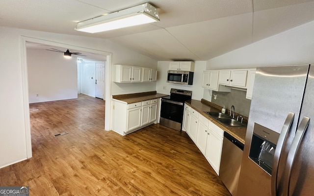 kitchen with stainless steel appliances, a sink, dark countertops, lofted ceiling, and white cabinetry