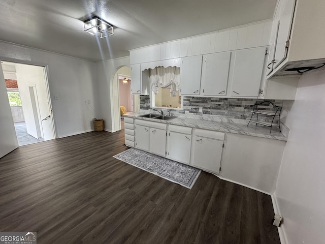 kitchen with dark wood-style floors, light countertops, decorative backsplash, arched walkways, and a sink