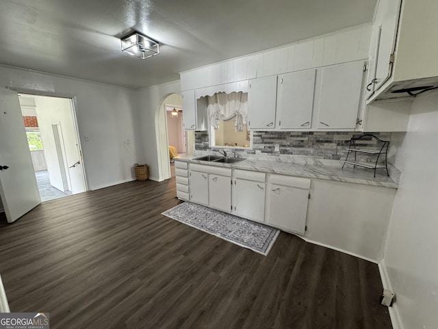 kitchen featuring backsplash, arched walkways, white cabinets, light countertops, and dark wood-style floors