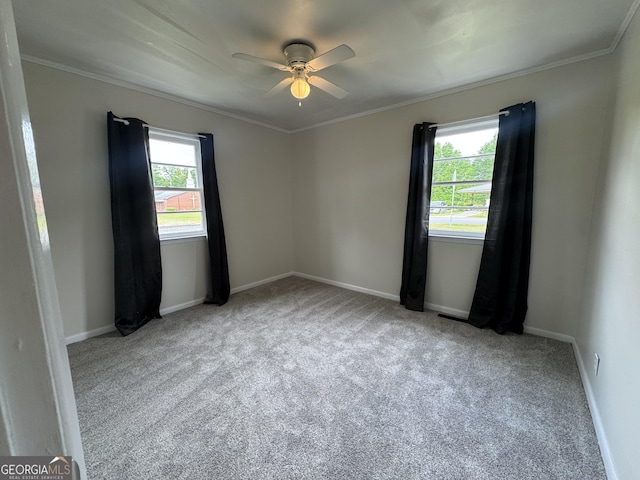 carpeted spare room featuring ornamental molding, baseboards, and a ceiling fan