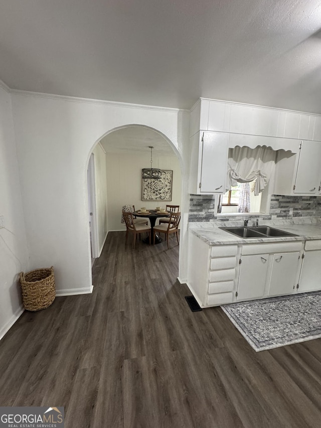 kitchen with light countertops, white cabinets, dark wood finished floors, arched walkways, and a sink