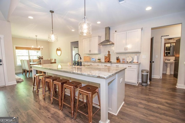 kitchen featuring dark wood-type flooring, wall chimney range hood, recessed lighting, a sink, and a breakfast bar area