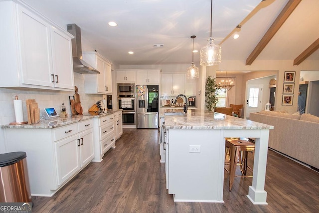 kitchen with white cabinets, wall chimney exhaust hood, open floor plan, appliances with stainless steel finishes, and a kitchen bar