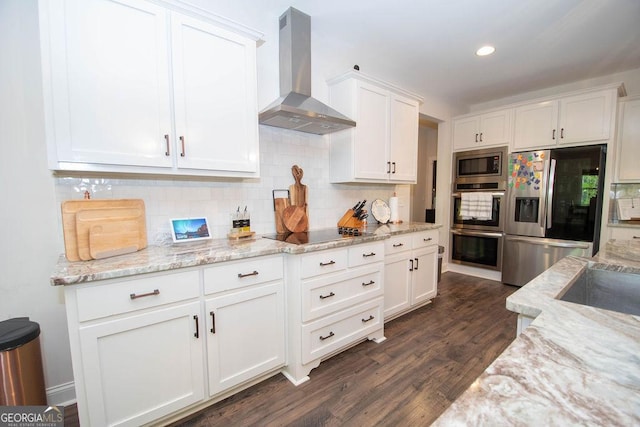 kitchen with wall chimney exhaust hood, dark wood-style flooring, white cabinetry, stainless steel appliances, and backsplash