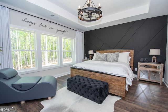 bedroom featuring visible vents, baseboards, a chandelier, a tray ceiling, and wood finished floors