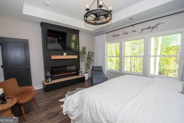 bedroom featuring visible vents, a tray ceiling, an inviting chandelier, and wood finished floors