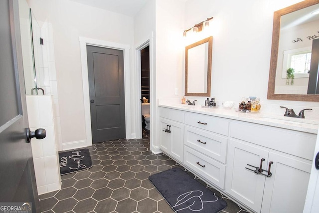 bathroom featuring a shower with shower door, double vanity, a sink, and toilet