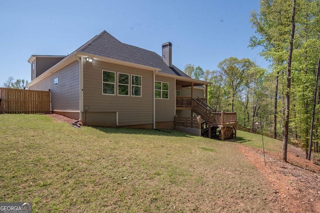 back of house with a chimney, stairway, a shingled roof, fence, and a lawn
