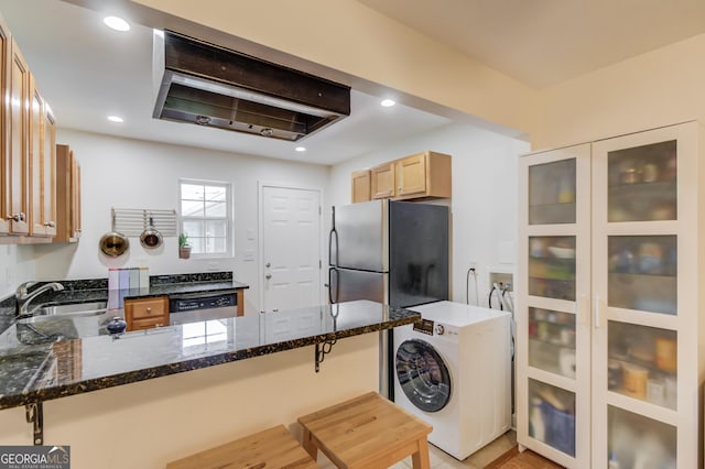 kitchen with a sink, washer / dryer, a peninsula, and dark stone countertops