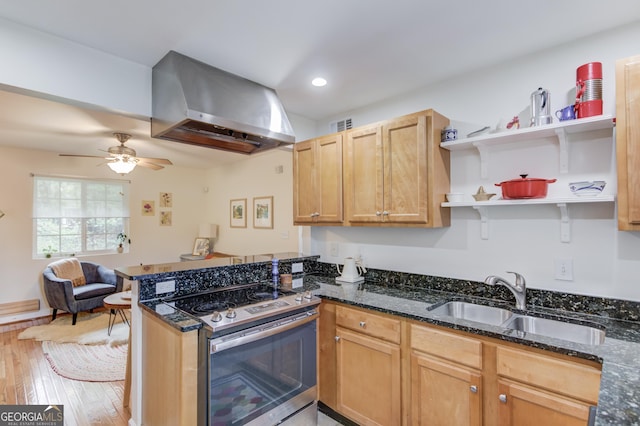 kitchen featuring wall chimney range hood, a sink, light wood-style floors, stainless steel range with electric stovetop, and a peninsula