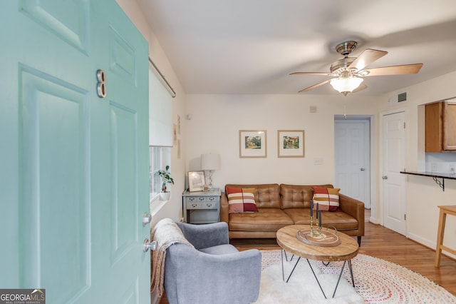 living room featuring ceiling fan, visible vents, baseboards, and light wood-style floors
