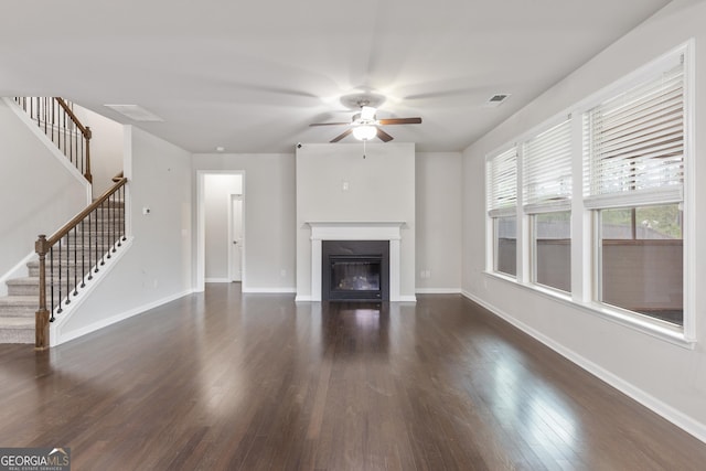 unfurnished living room with a ceiling fan, a glass covered fireplace, stairway, and dark wood finished floors