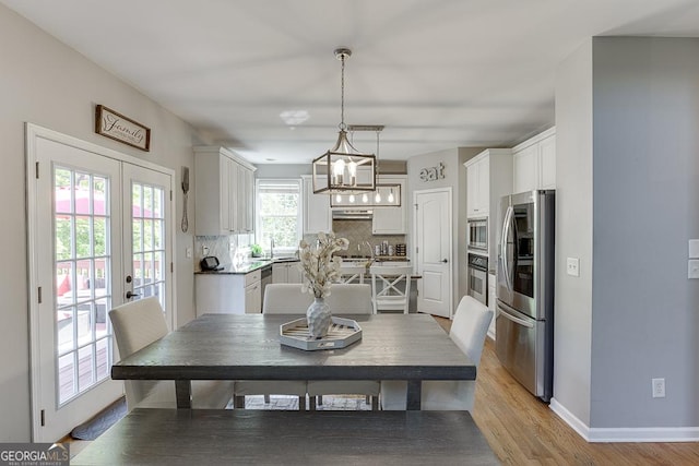 dining area featuring light wood-style flooring, french doors, baseboards, and a notable chandelier
