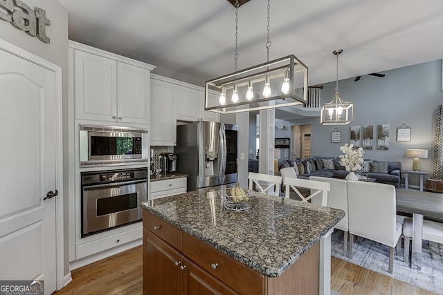 kitchen featuring white cabinets, open floor plan, appliances with stainless steel finishes, light wood finished floors, and a kitchen island