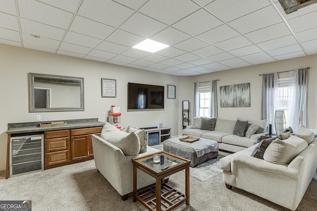 carpeted living area with a paneled ceiling and beverage cooler