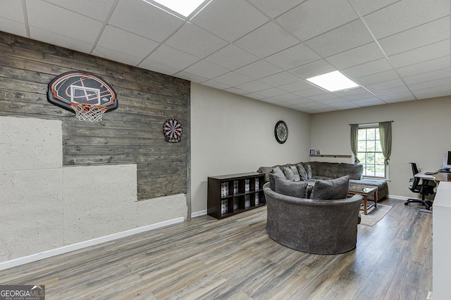 living room with baseboards, an accent wall, a paneled ceiling, wood finished floors, and wood walls