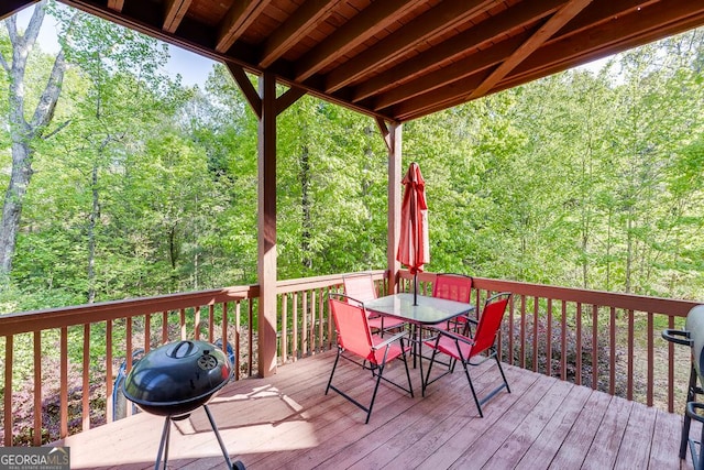 wooden terrace with area for grilling, outdoor dining space, and a forest view