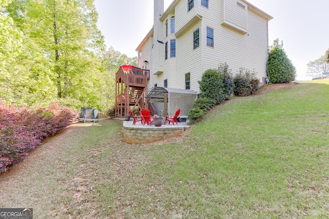 exterior space featuring a deck, an outdoor fire pit, a trampoline, a patio, and stairs