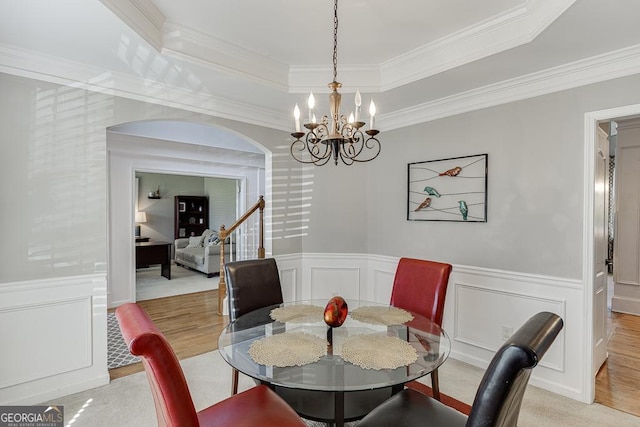 dining area with a decorative wall, a chandelier, crown molding, a tray ceiling, and wainscoting