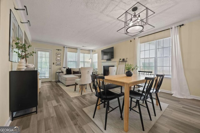 dining area featuring a fireplace, a textured ceiling, baseboards, and wood finished floors