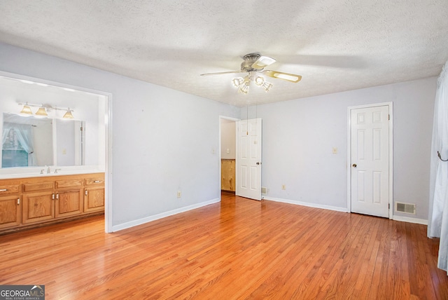 unfurnished bedroom featuring a textured ceiling, a sink, visible vents, baseboards, and light wood finished floors