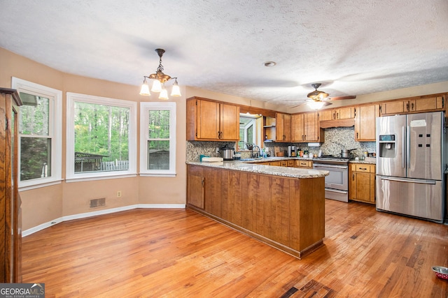 kitchen with light wood finished floors, stainless steel appliances, decorative backsplash, brown cabinetry, and a peninsula