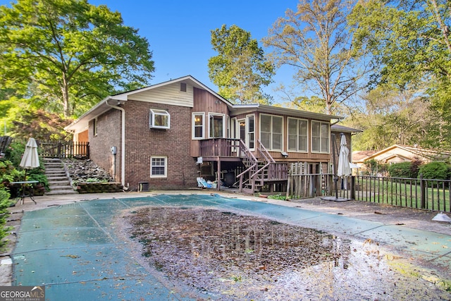 rear view of house featuring a sunroom, a fenced in pool, stairs, brick siding, and fence