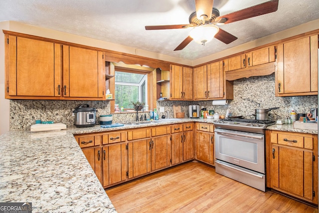 kitchen featuring stainless steel gas range, a sink, open shelves, brown cabinetry, and light wood-style flooring