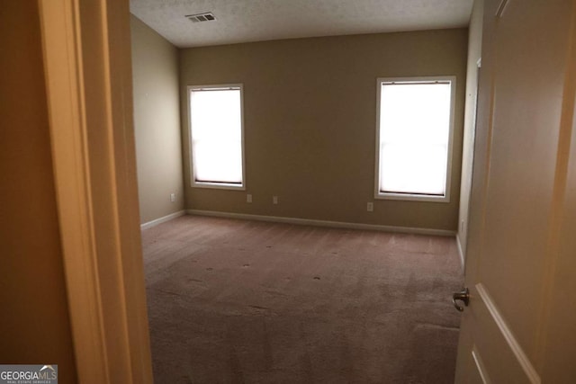 unfurnished room with visible vents, baseboards, carpet flooring, and a textured ceiling