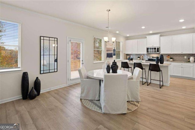 dining space featuring crown molding, light wood finished floors, a notable chandelier, and baseboards