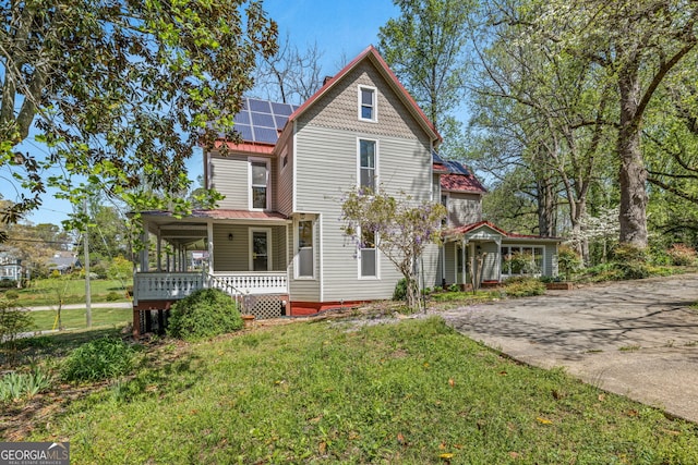 victorian house featuring a front yard, a porch, and solar panels