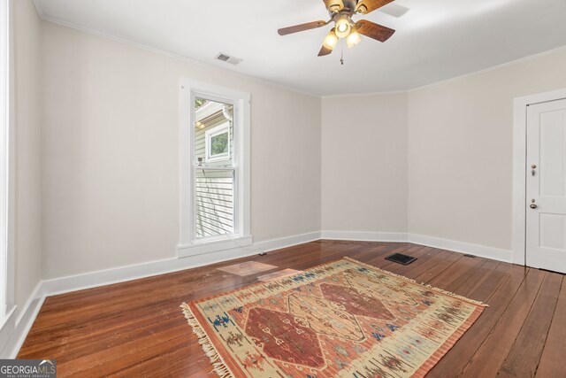 empty room featuring wood-type flooring, ornamental molding, and visible vents