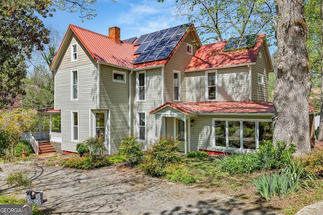 back of house featuring a chimney and solar panels