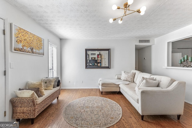 living room with an inviting chandelier, a textured ceiling, visible vents, wood finished floors, and baseboards