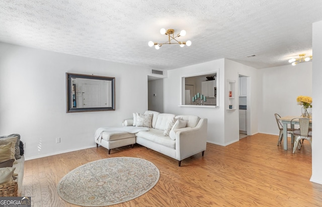 living area with a chandelier, light wood-style floors, visible vents, and a textured ceiling