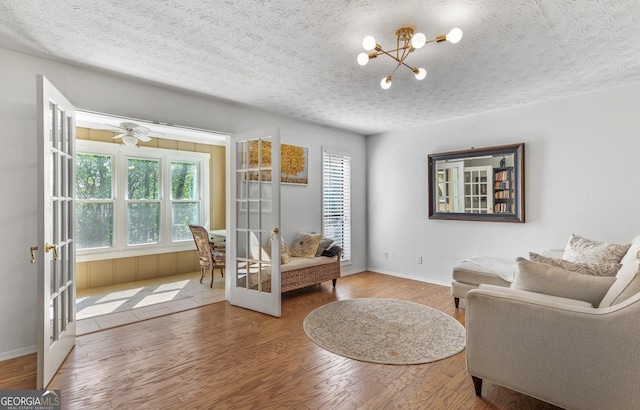 sitting room with a notable chandelier, baseboards, french doors, a textured ceiling, and wood finished floors