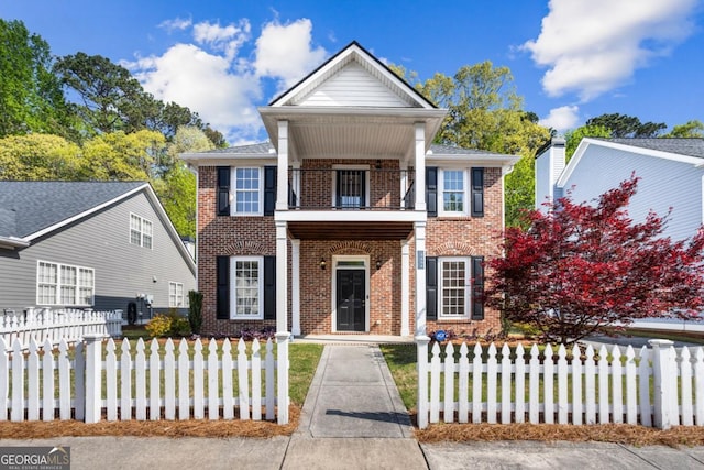 neoclassical home with brick siding, fence, and a balcony