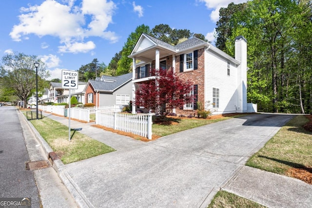view of front of house featuring a balcony, a chimney, driveway, brick siding, and fence