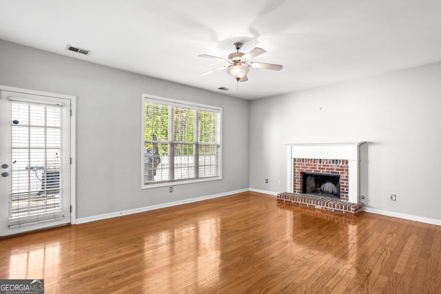 unfurnished living room featuring a ceiling fan, visible vents, wood finished floors, a brick fireplace, and baseboards