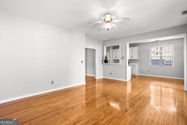 unfurnished living room featuring light wood-style floors, ceiling fan with notable chandelier, baseboards, and visible vents