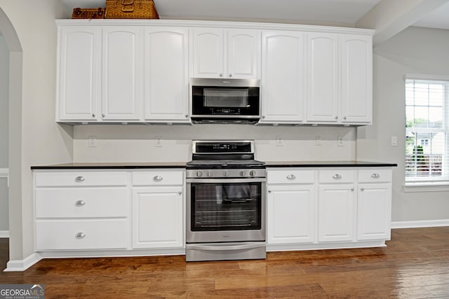 kitchen with arched walkways, dark countertops, appliances with stainless steel finishes, and white cabinetry