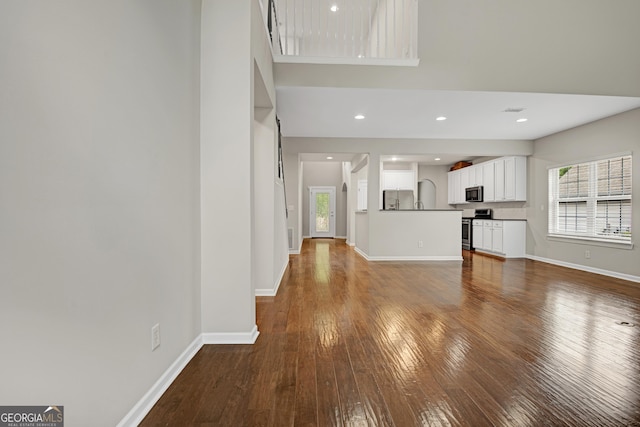 unfurnished living room with baseboards, dark wood-type flooring, and a healthy amount of sunlight