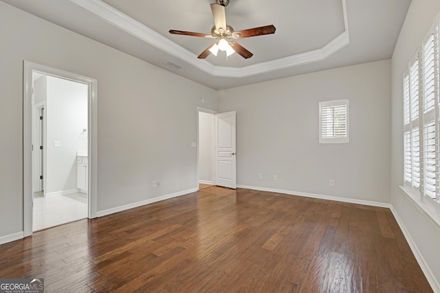 unfurnished bedroom featuring a tray ceiling, visible vents, baseboards, wood finished floors, and ornamental molding